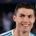 "Cristiano Ronaldo smiling and waving to fans during a match, wearing his iconic football jersey, representing one of the greatest footballers of all time."